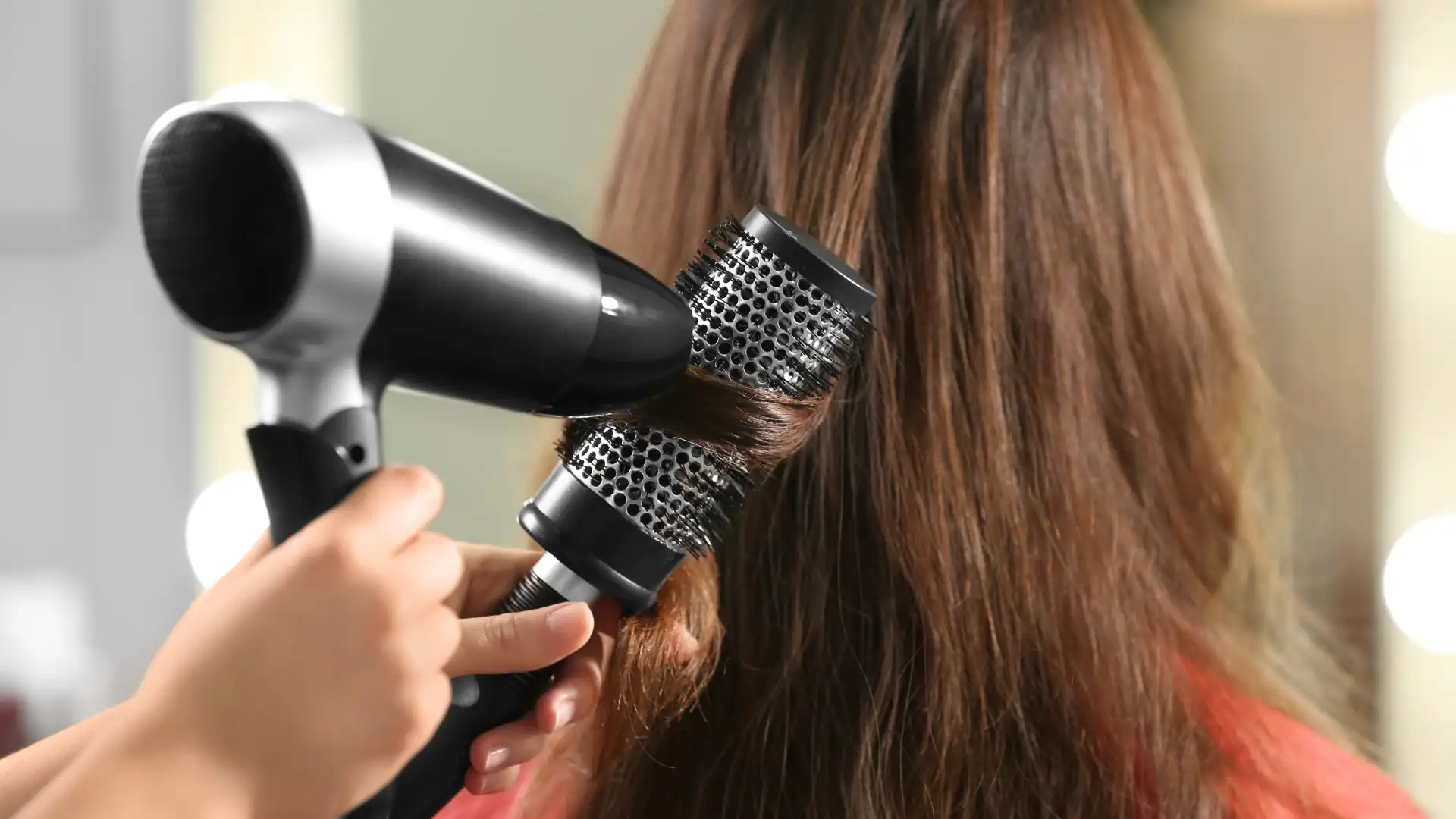 A person blow-drying brown hair using a round brush.